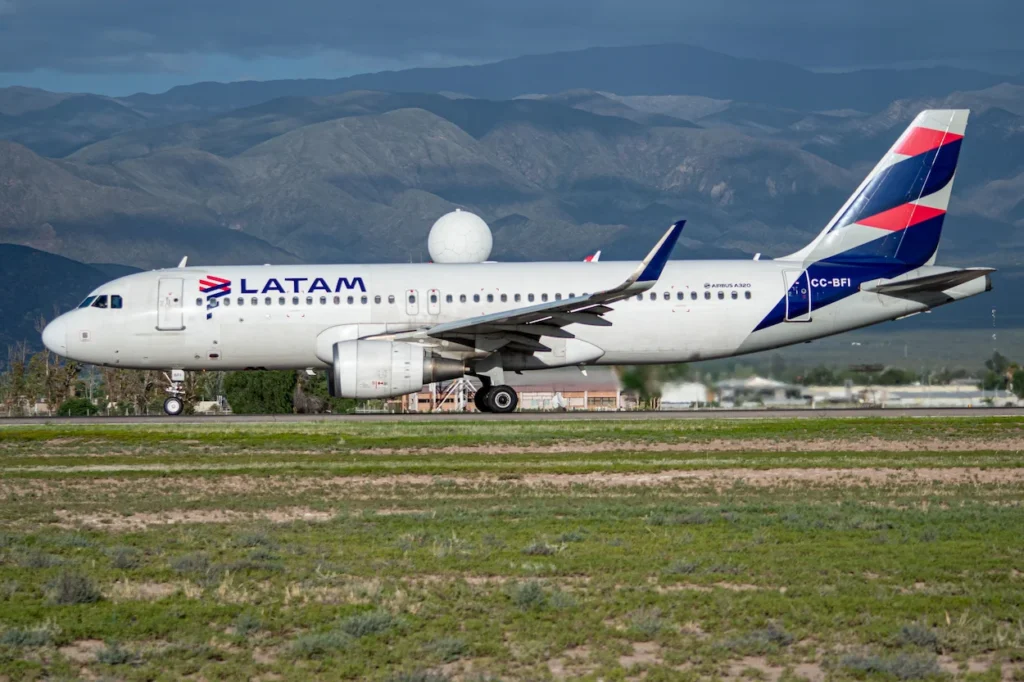 A LATAM Airlines Airbus A320 taxiing on a runway with arid, rolling mountains in the background