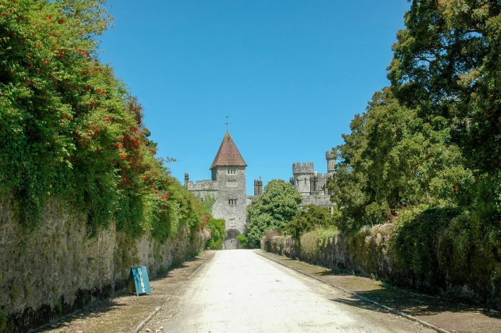 Gravel driveway leading toward the stone towers of Lismore Castle under a clear blue sky