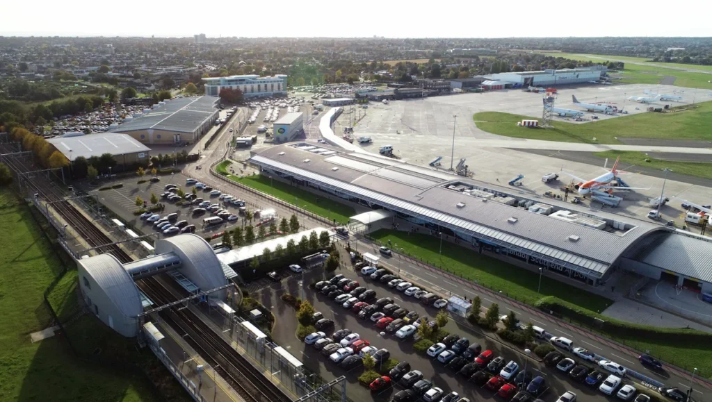 Aerial view of London Southend Airport terminal building, parking lots, tarmac, and an adjacent train station