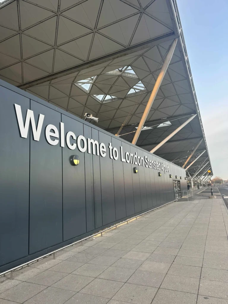 Welcome to London Stansted Airport sign on a black wall under a geometric glass and steel canopy