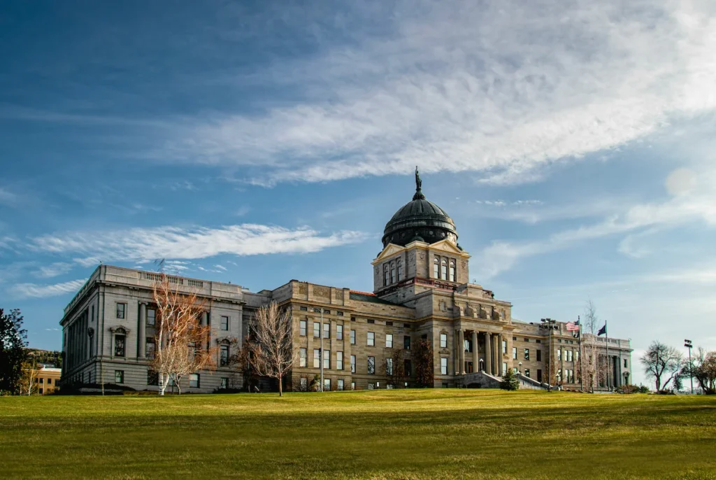 Montana State Capitol building with its dark copper dome and stone facade under a blue sky in Helena