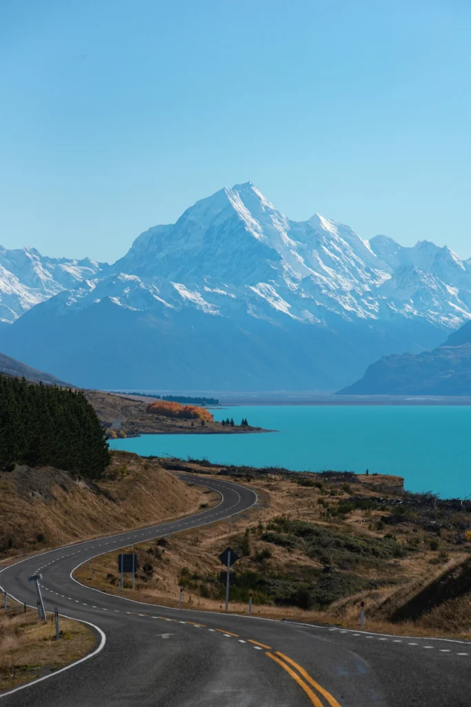 Winding asphalt road leading toward the turquoise Lake Pukaki and snow-capped Mount Cook
