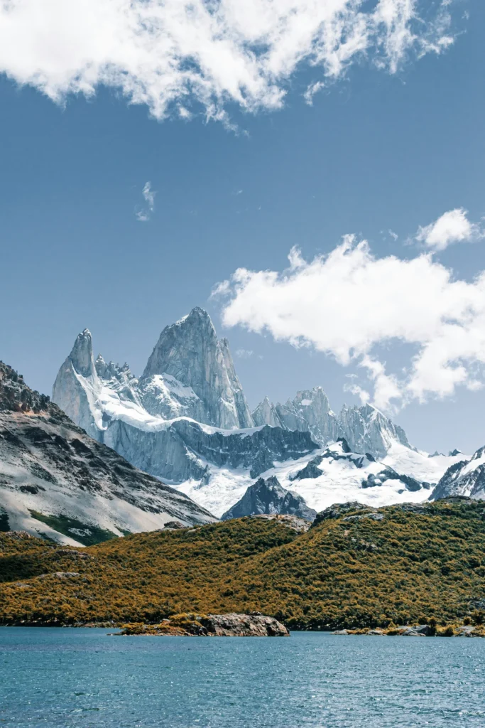 Snow-covered peaks of Mount Fitz Roy behind a blue lake and golden hills