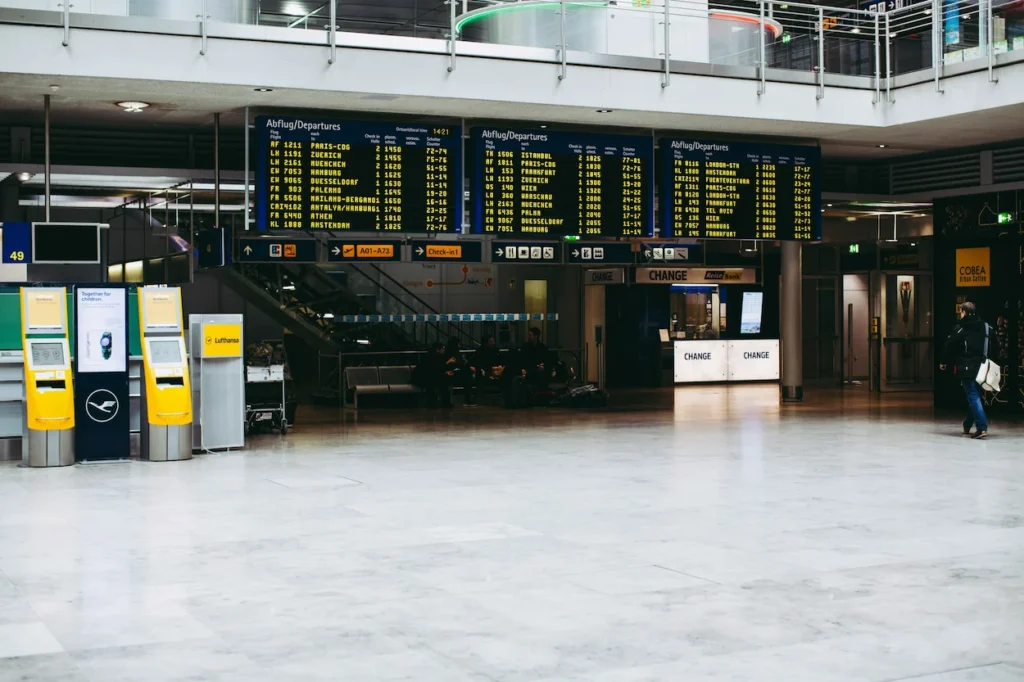 Three large flight departure boards above yellow Lufthansa check-in kiosks in the terminal hall