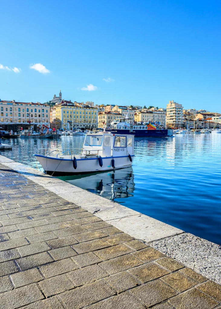 Small white fishing boat moored along a stone pier in the Vieux Port of Marseille under a clear blue sky