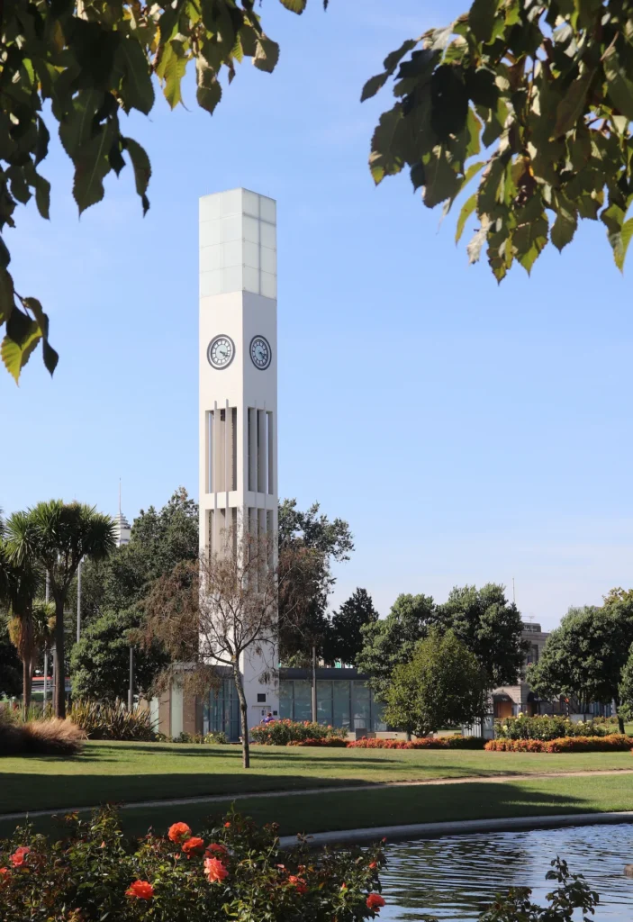 Hopwood Clock Tower with illuminated glass top behind a pond and blooming orange roses