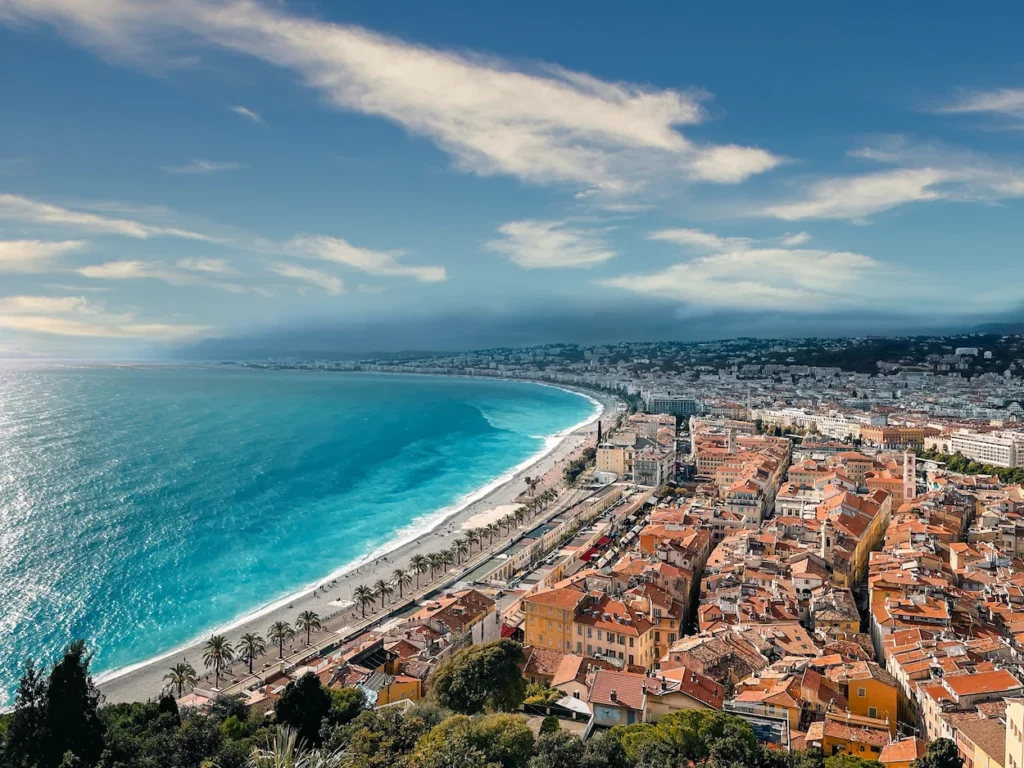 High-angle view of the turquoise coast, curved beach, and city buildings in Nice, France