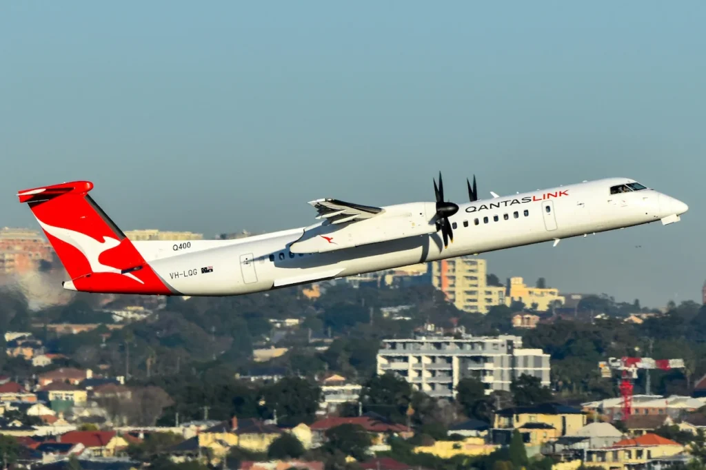 QantasLink Dash 8 Q400 turboprop plane ascending sharply over a suburban cityscape