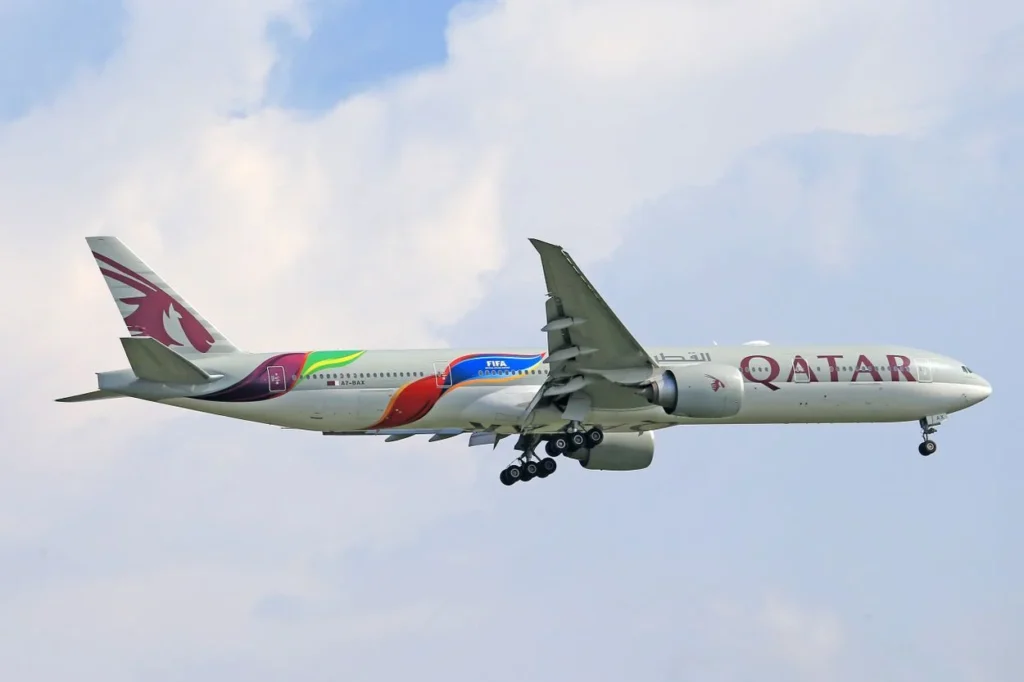 A Qatar Airways Boeing 777-300ER in special FIFA livery flying with landing gear down