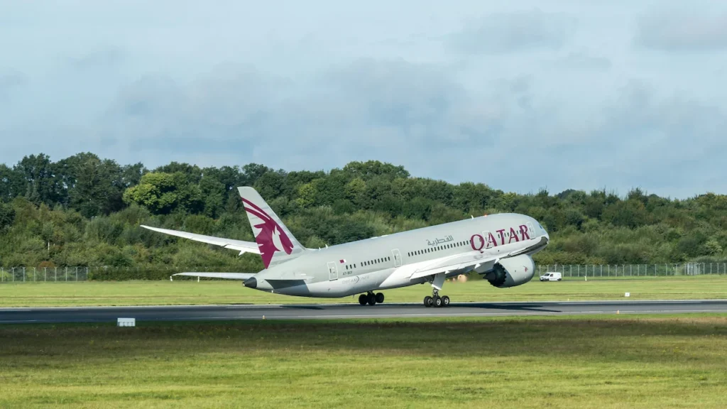 Qatar Airways Boeing 787 Dreamliner lifting off the runway during takeoff with green trees in the background