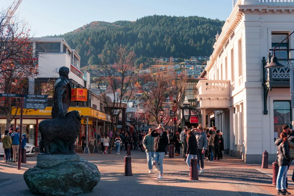 Bronze statue on a busy Queenstown pedestrian street with forested hills behind