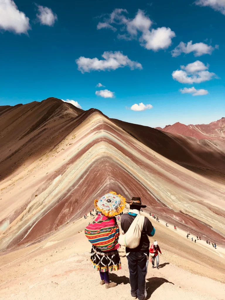 Two hikers in traditional Andean clothing looking at Vinicunca Rainbow Mountain in Peru