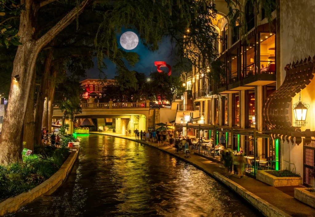 San Antonio River Walk at night with illuminated waterfront restaurants and trees reflecting on the water