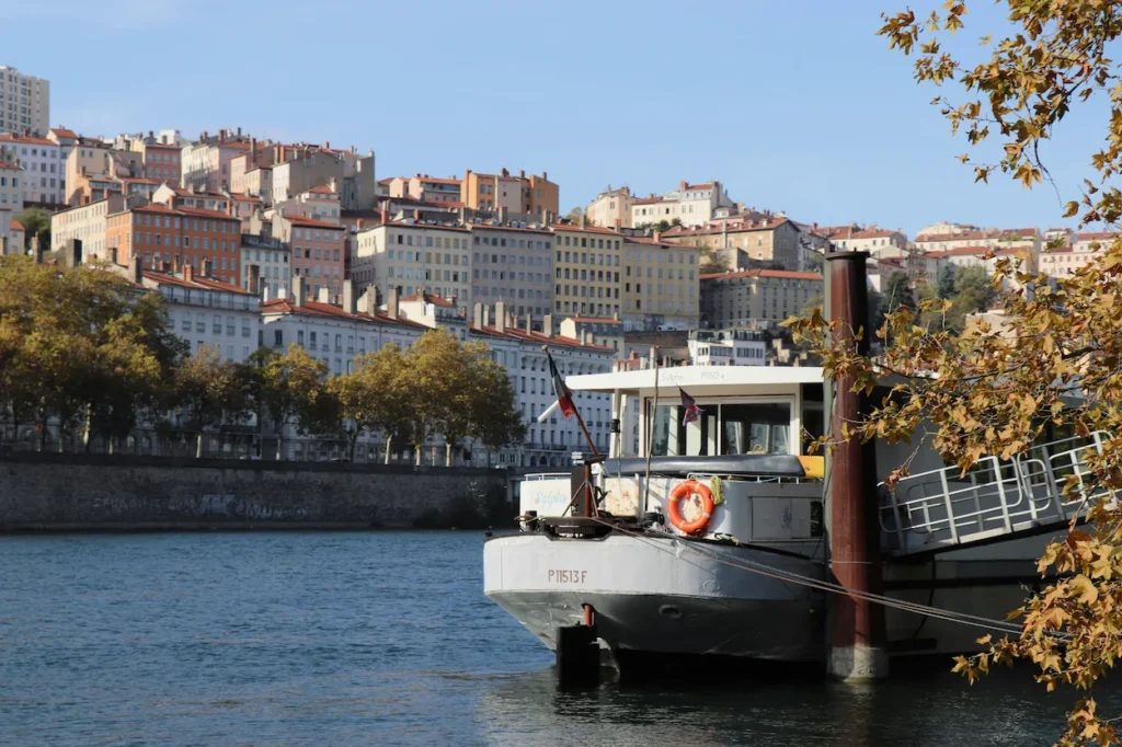 Riverboat docked on the Saône River with the dense Croix-Rousse hillside buildings of Lyon in the background
