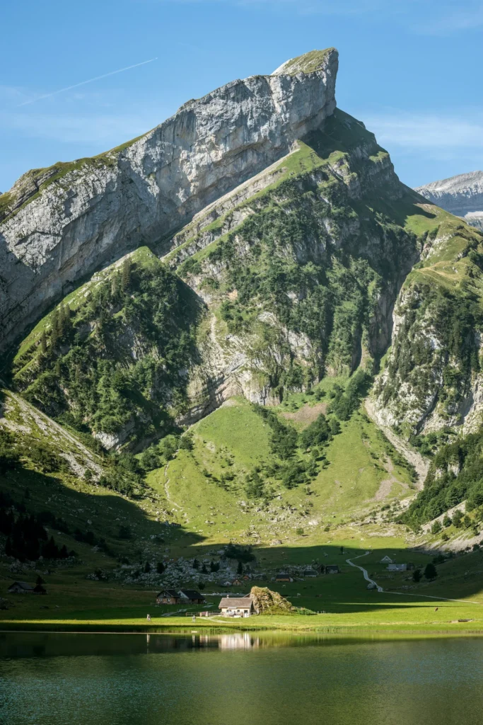 Sharp limestone mountain peak rising above rustic alpine wooden cabins near Seealpsee shoreline in Appenzell, Switzerland