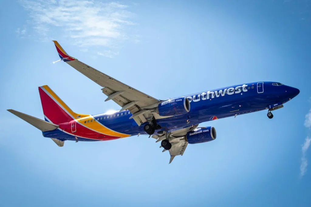 A blue, yellow, and red Southwest Airlines Boeing 737 passenger plane soaring overhead against a clear blue sky