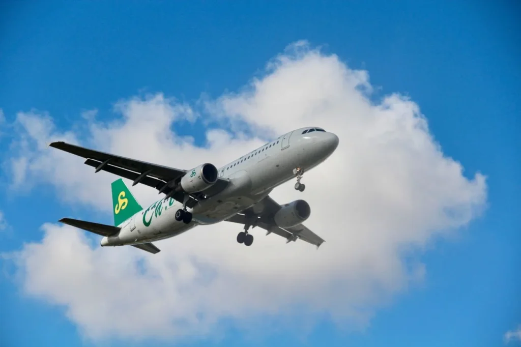 A green and white Spring Airlines airplane flying below white clouds