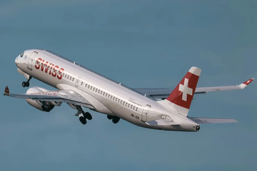 SWISS International Air Lines Airbus A220-300 passenger airplane banking and climbing into a hazy blue sky