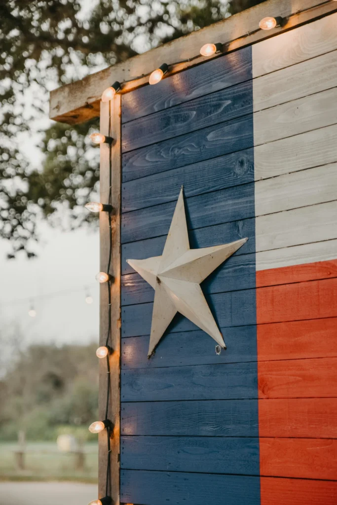 Rustic wooden wall painted like the Texas state flag with a metal lone star and string lights