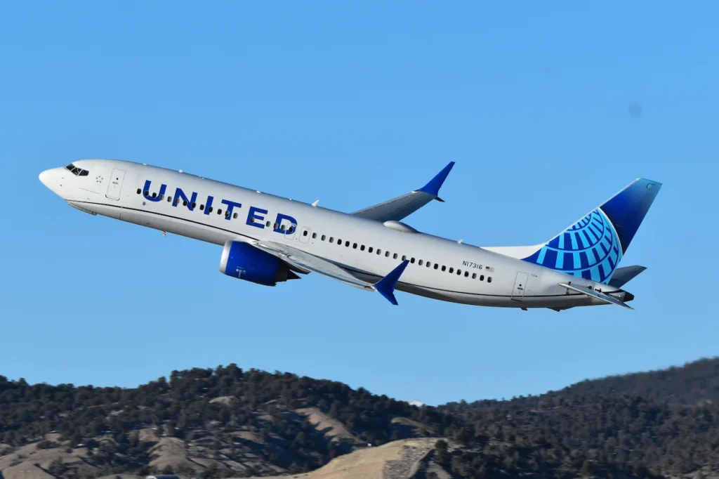United Airlines Boeing 737 MAX 9 passenger plane with tail number N17316 climbing over hills during takeoff