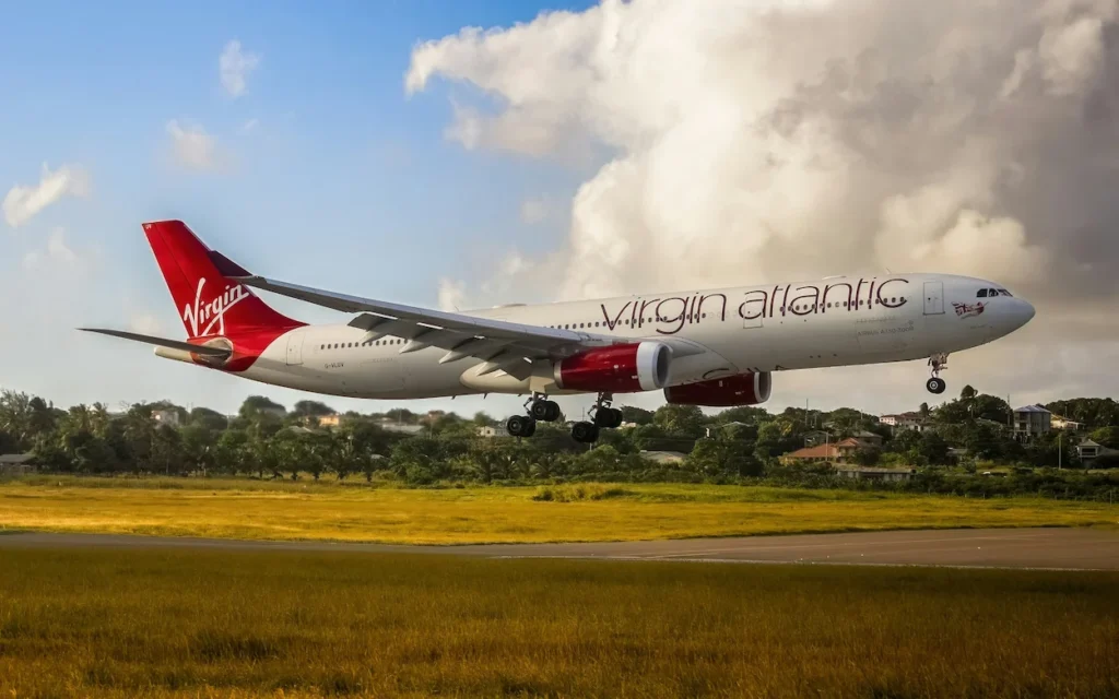 Virgin Atlantic Airbus A330 passenger plane landing over a grassy field with trees