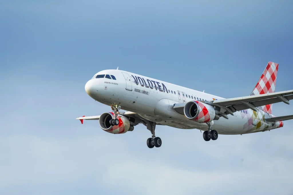 Volotea Airbus A320 commercial passenger airplane on landing approach with landing gear down against a light blue sky