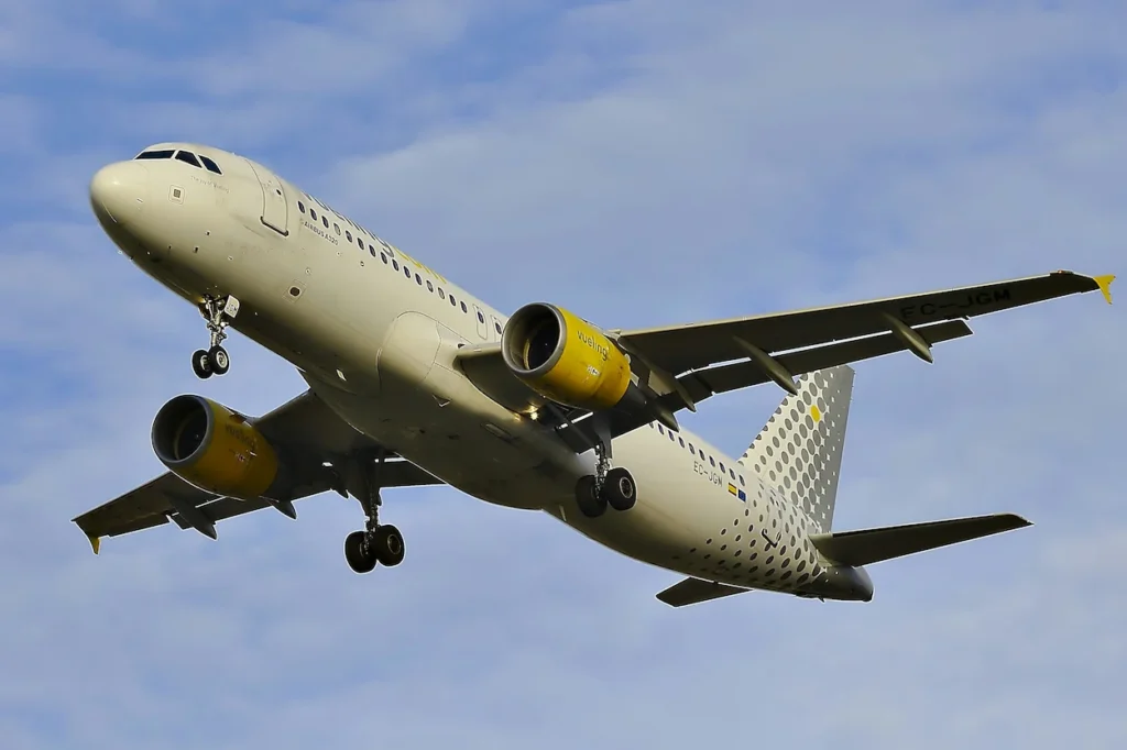 A Vueling Airlines Airbus A320 with landing gear down descending against a blue sky with light clouds