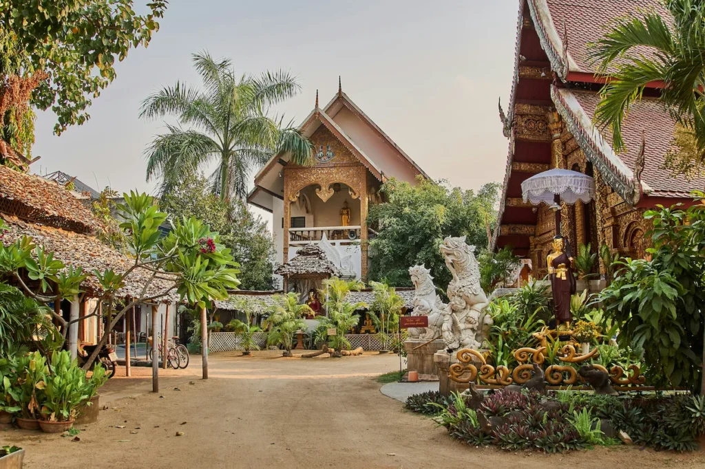 White lion guardian statues standing along a dirt courtyard pathway inside Wat Mahawan in Chiang Mai, Thailand
