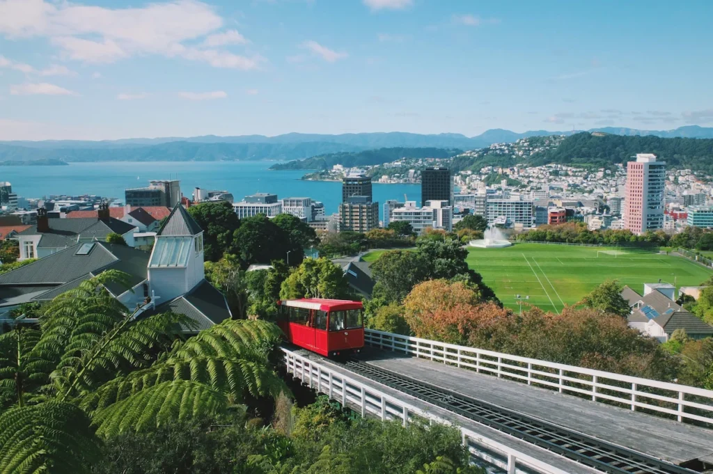 A red cable car climbing a hill tracks overlooking Wellington city and the harbor under a clear sky