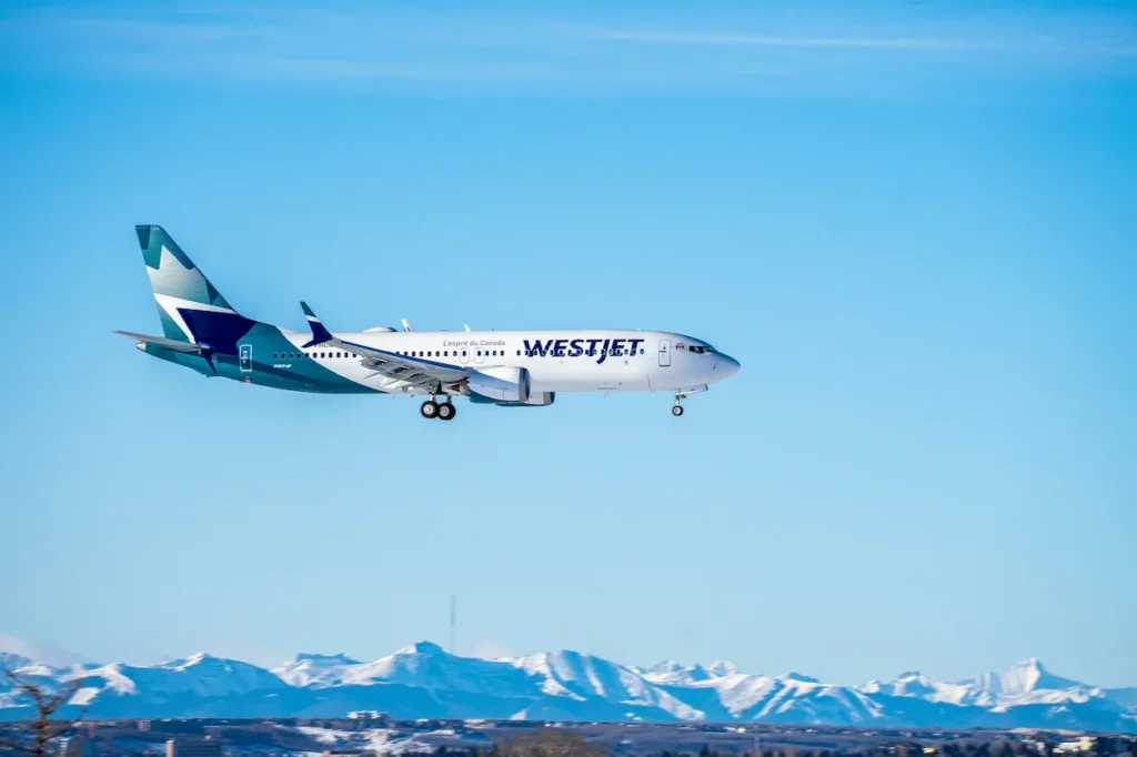 WestJet Boeing 737 MAX 8 descending with landing gear down against snow-capped mountains