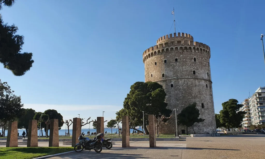 White Tower of Thessaloniki standing next to a waterfront promenade under a blue sky