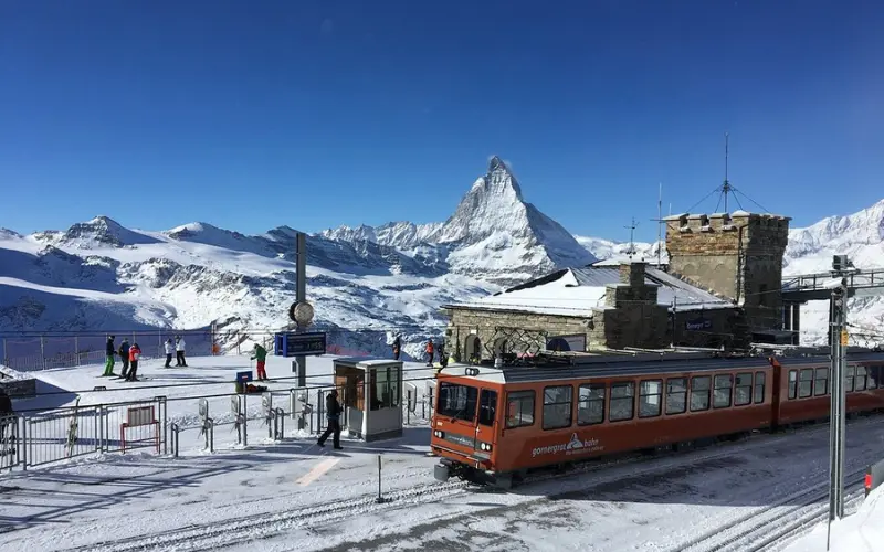Matterhorn, Zermatt shows a red train station with snowy mountains and the iconic Matterhorn peak in the background.