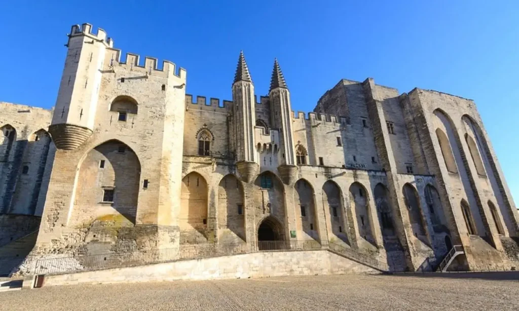 The Palace of the Popes in Avignon with its grand medieval stone facade under a clear blue sky.