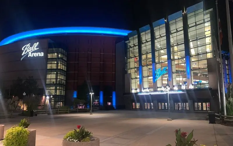 The glass and brick exterior of Ball Arena is lit up at night.
