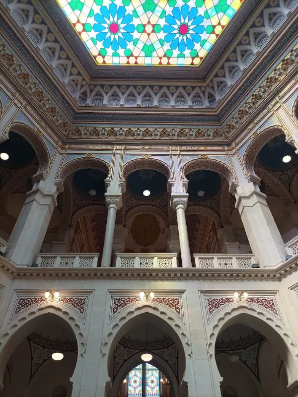 Ornate interior of Sarajevo’s City Hall with arched balconies and a colorful stained-glass ceiling.