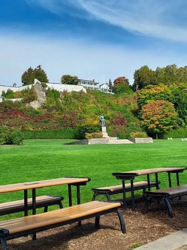 A statue stands in the center of Marquette Park with Fort Mackinac on the hill above.