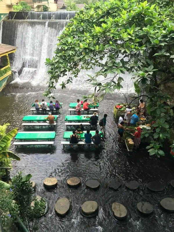 Guests dine at tables in shallow water beneath a waterfall at Villa Escudero Plantation.
