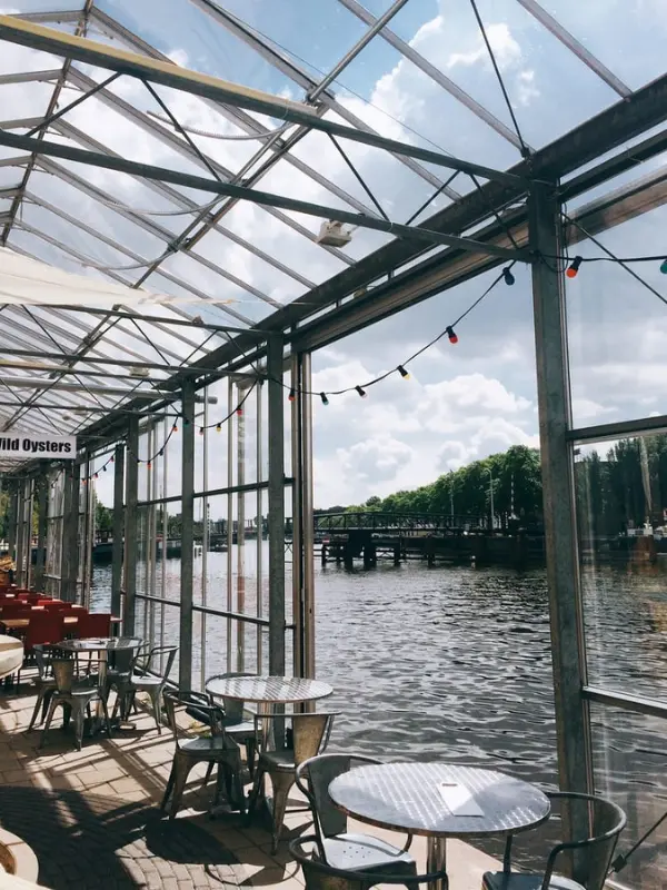 Outdoor seating by the water at Mediamatic ETEN with glass walls and string lights.