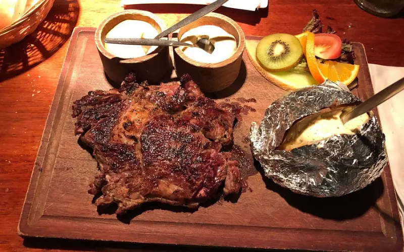 Grilled steak with sauces, baked potato, and fruit garnish at Castell.