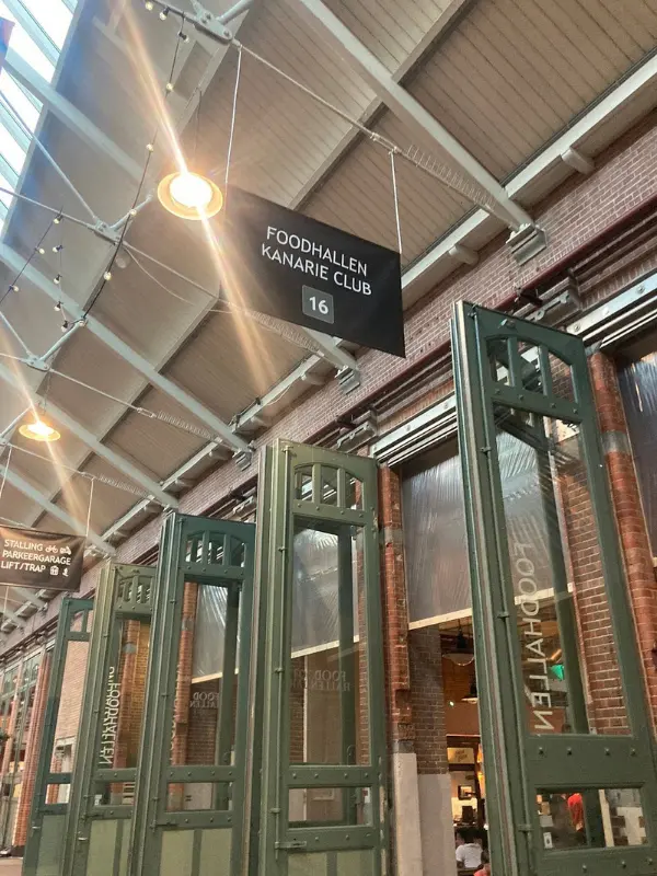 High-ceilinged indoor Foodhallen market with green doors and signage.