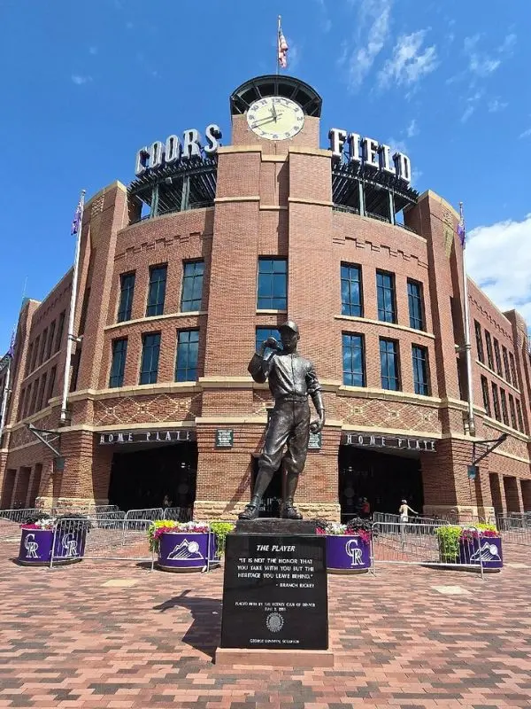 The statue in front of Coors Field stands before the brick stadium entrance.