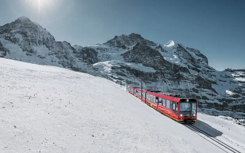 Jungfrau, Bernese Oberland displays a red cogwheel train climbing through snow near the Jungfrau massif.