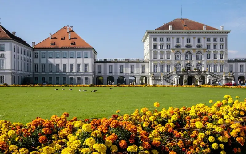 Front view of Nymphenburg Palace with a garden of yellow flowers.