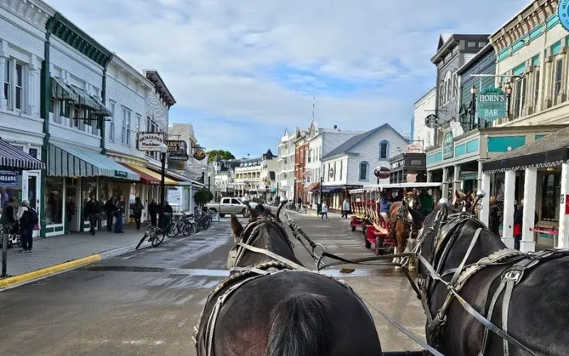 Horse-drawn carriages pass shops along the main street during Mackinac Island Carriage Tours.