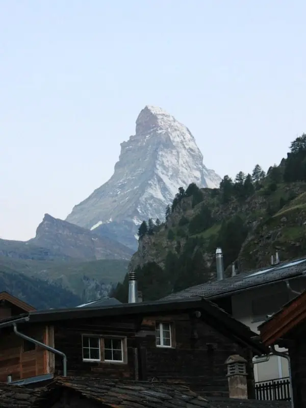 Weisshorn rises dramatically behind wooden alpine chalets in a quiet mountain village.