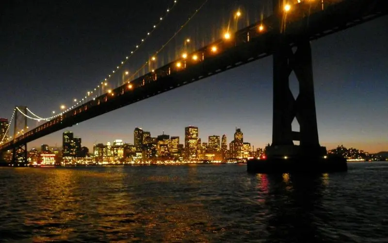 Bay Bridge lights shining over the water at dusk.