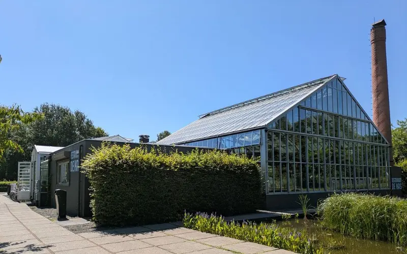 Glass greenhouse building of De Kas restaurant surrounded by greenery.