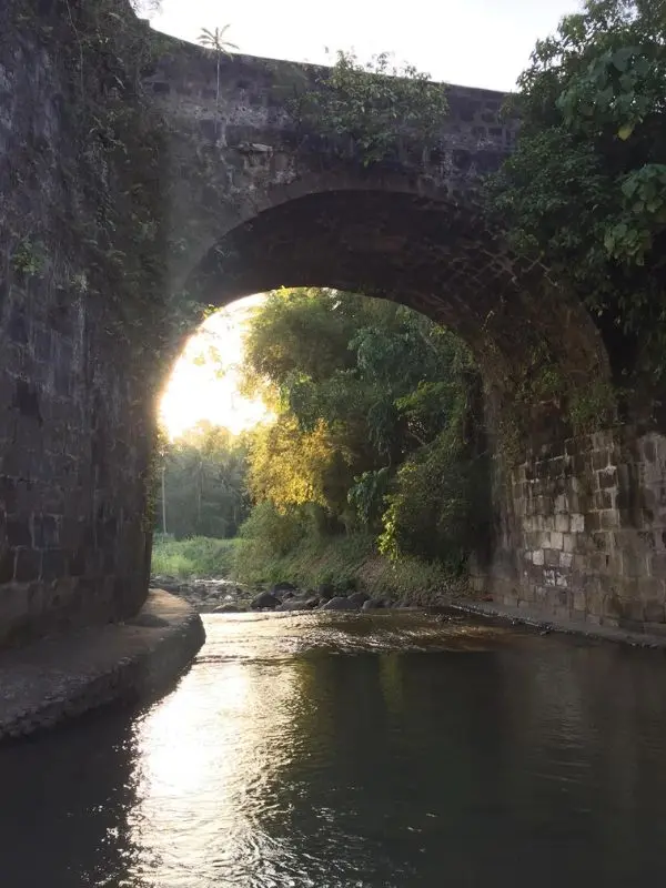 The stone arch of Malagonlong Bridge spans a shallow river.