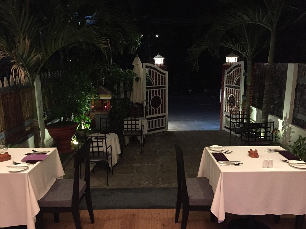 Outdoor evening dining at Aubergine49 with white tablecloths and lantern-lit palm surroundings.