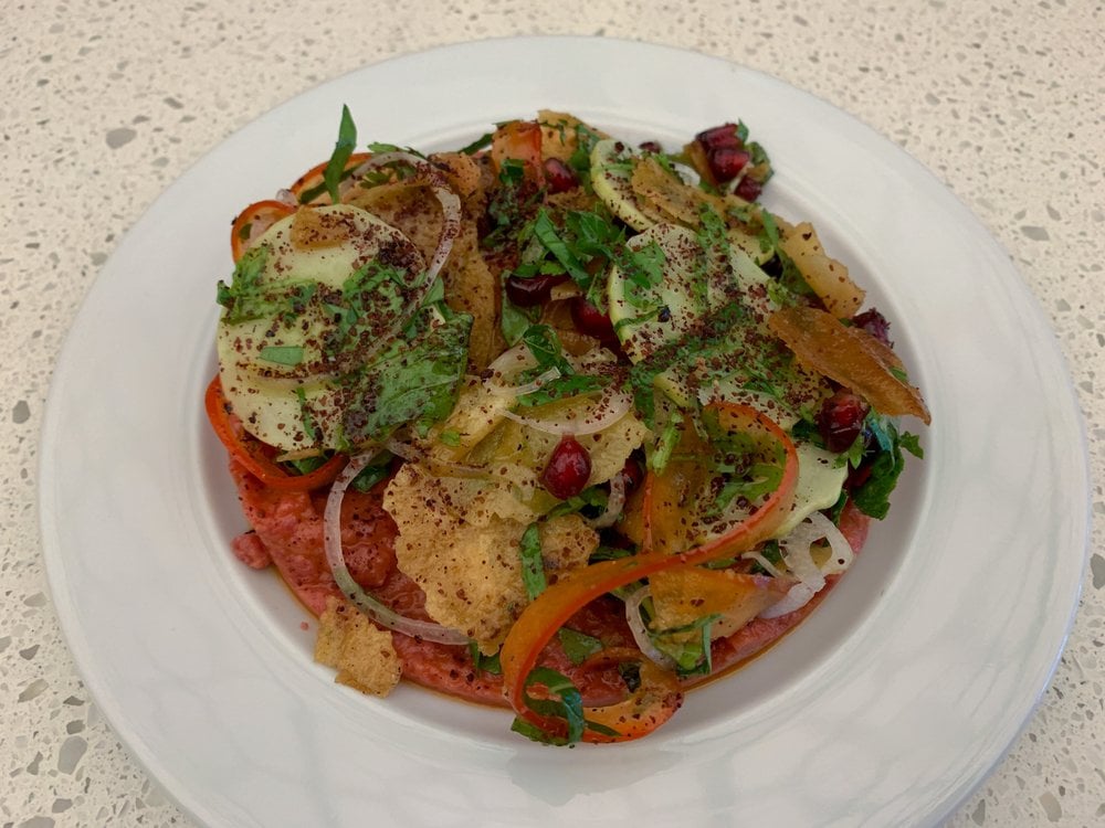 A colorful dish at BAR ST-DENIS topped with fresh herbs, avocado, and pomegranate seeds on a white plate.